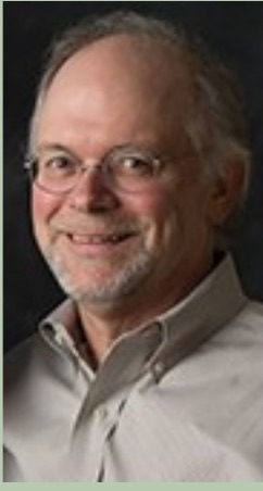 Marc DeLong, wearing glasses and a light shirt, against a dark background.