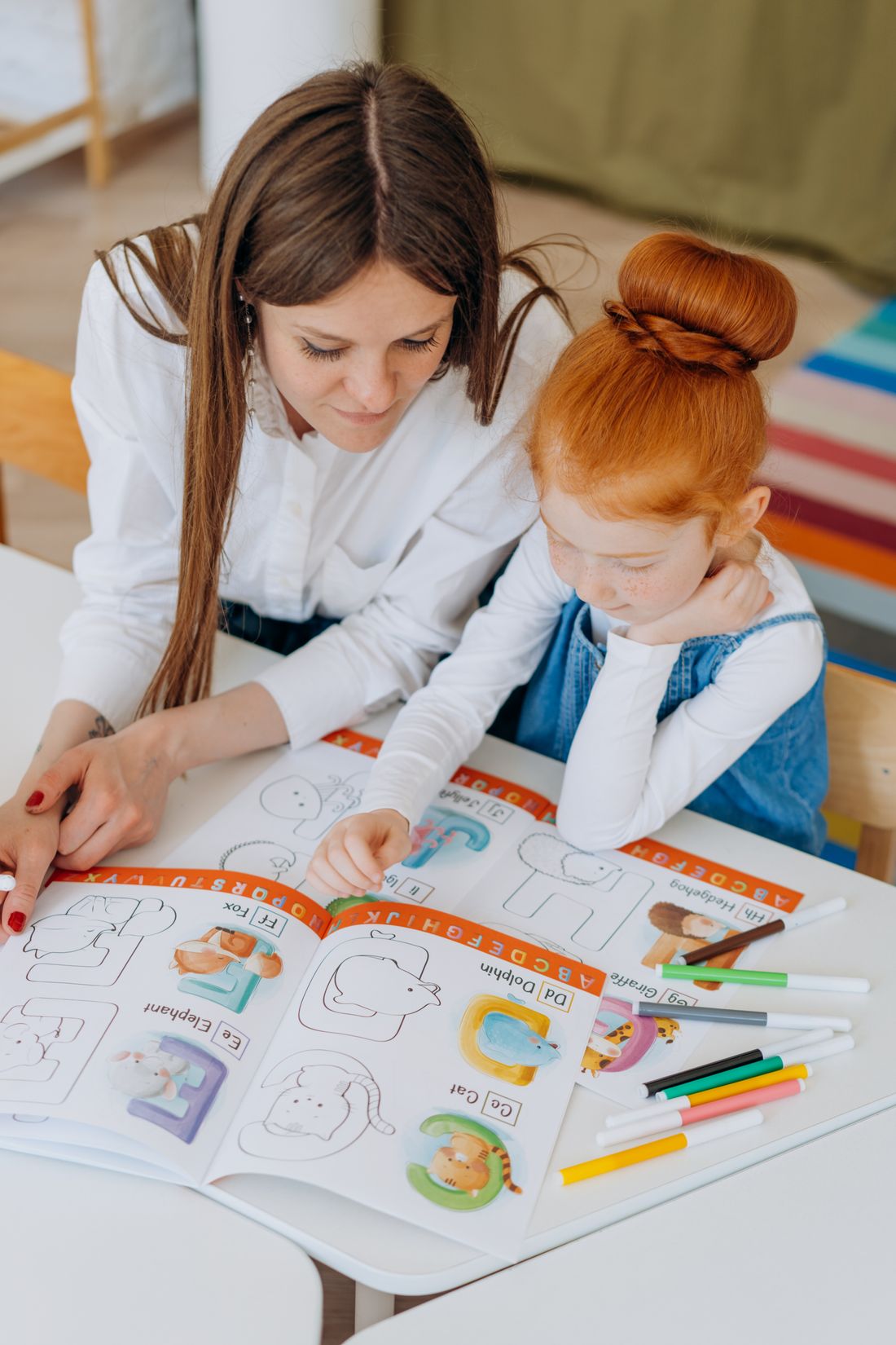 A tutor guiding a child's hand as she writes at the table