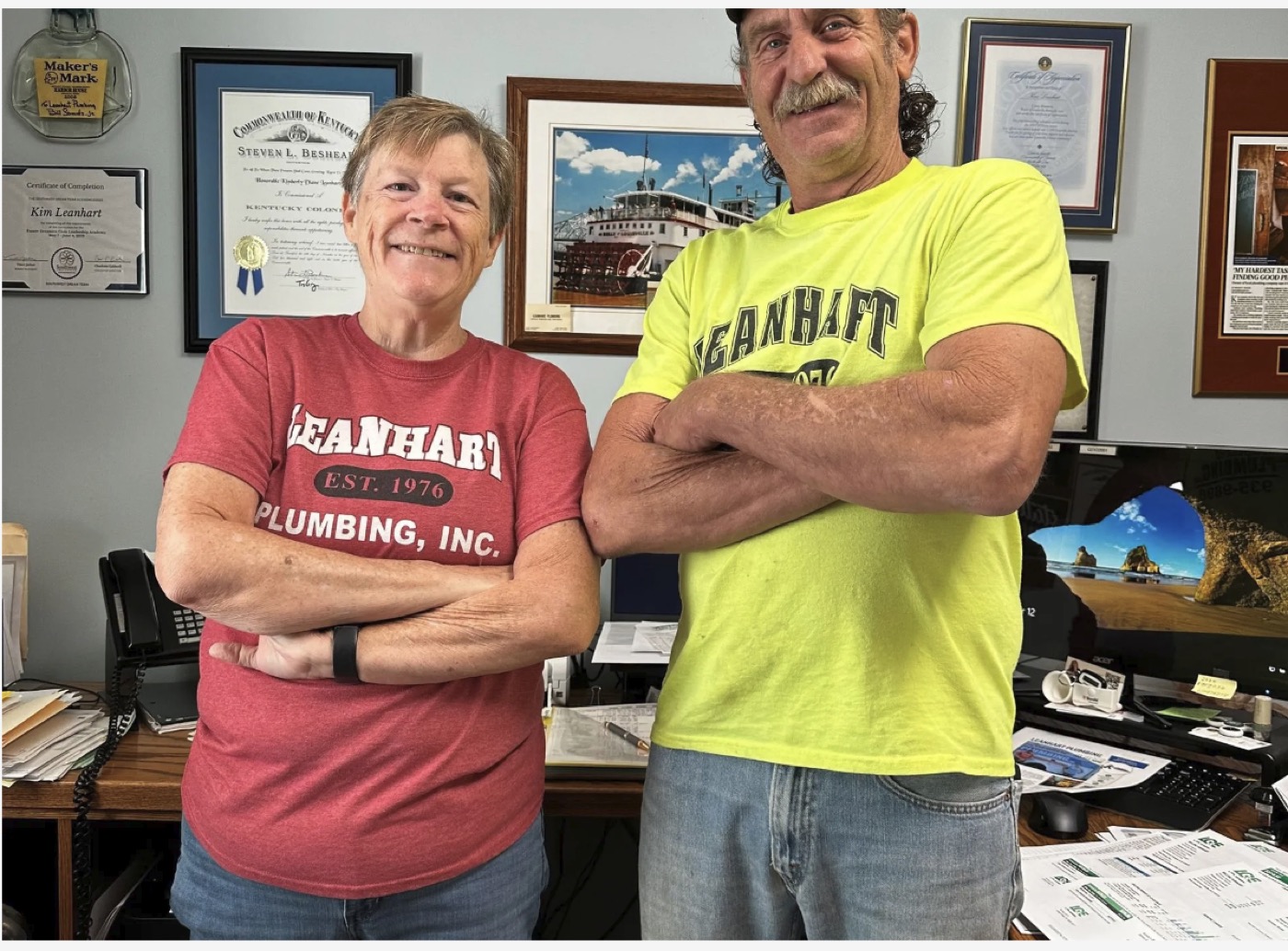 The Leanhart owners standing together in their Louisville office, framed certificates on the wall behind them