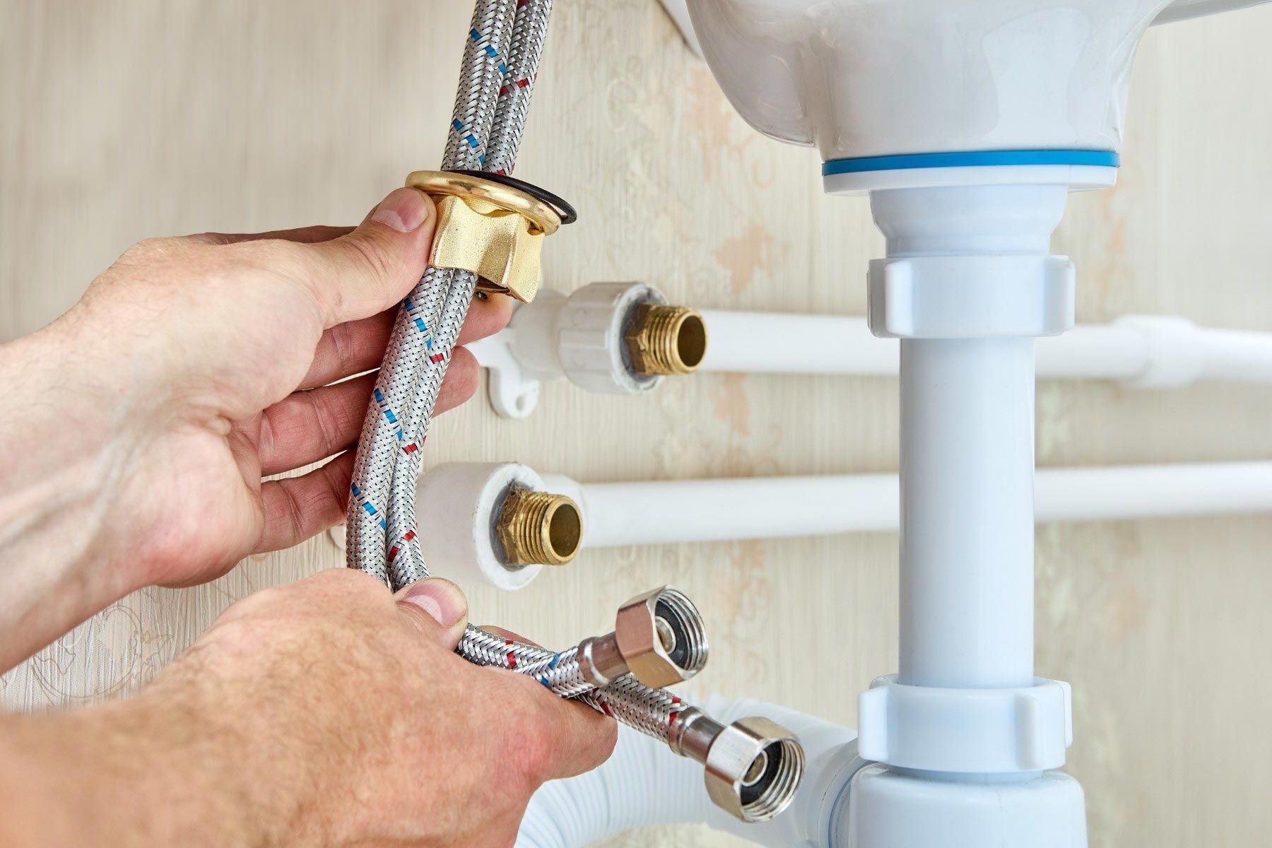 A plumber connecting supply lines under a sink during an installation