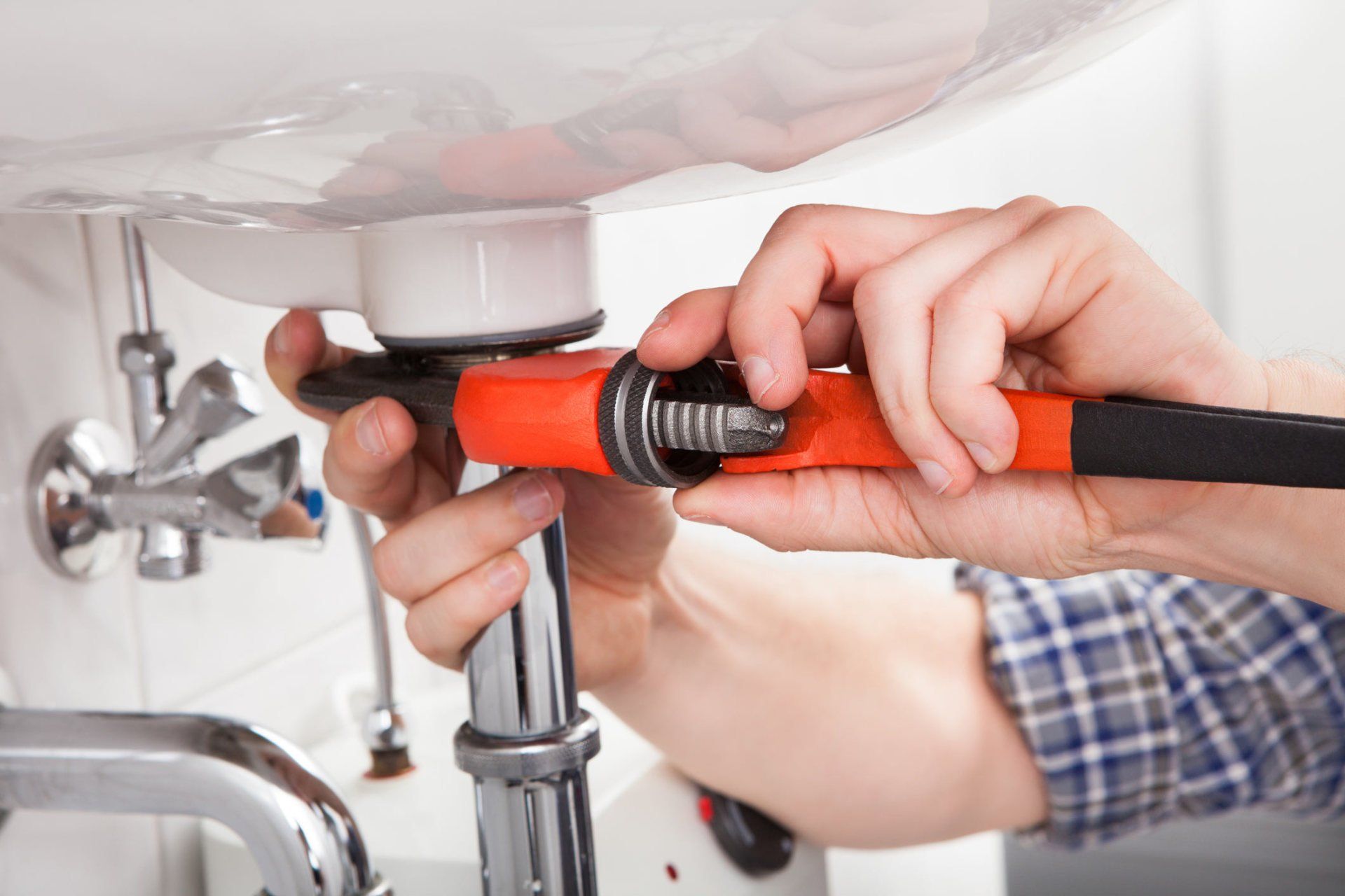 Plumber using a pipe wrench on a chrome drain trap under a sink